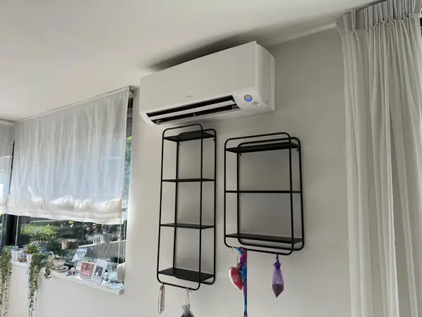 Wit Daikin airco-binnendeel boven twee wandrekken in een woonkamer