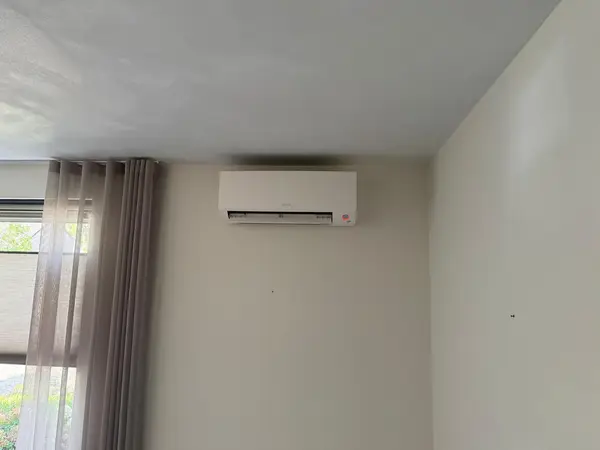 Daikin-binnendeel hoog op een lichte wand naast het raam