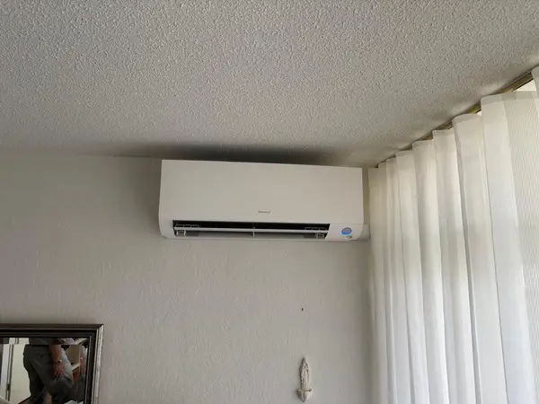 Wit Daikin airco-binnendeel onder een structuurplafond naast vitrage