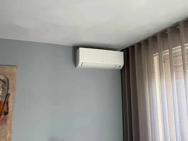 Daikin-binnendeel op een blauwgrijze wand naast de gordijnen