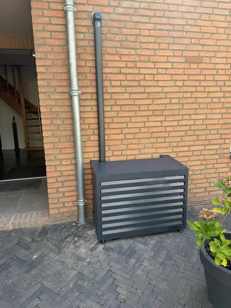 Antracietkleurige omkasting rond een buitenunit tegen een bakstenen gevel