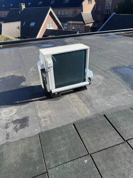 Buitenunit op dempers op een plat dak, met woningen op de achtergrond