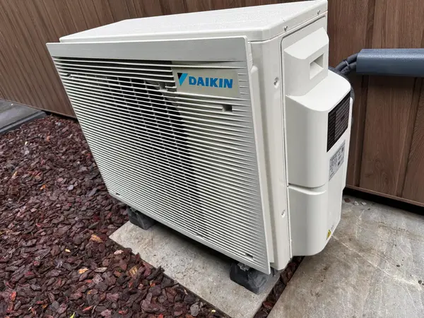 Daikin-buitenunit op trillingsdempers naast een houten gevel